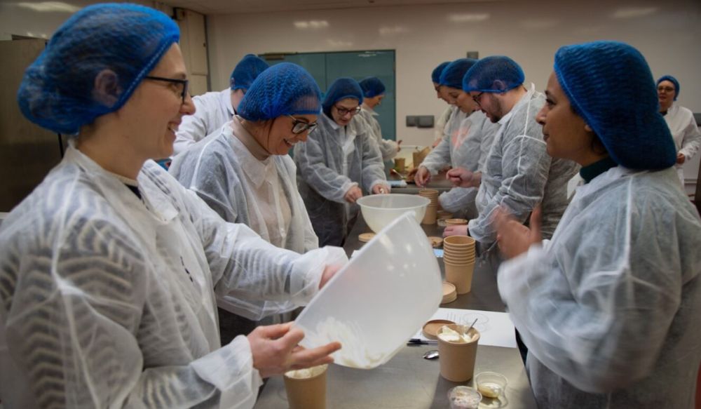 Group of people in a commercial style kitchen wearing blue hair nets and white overalls